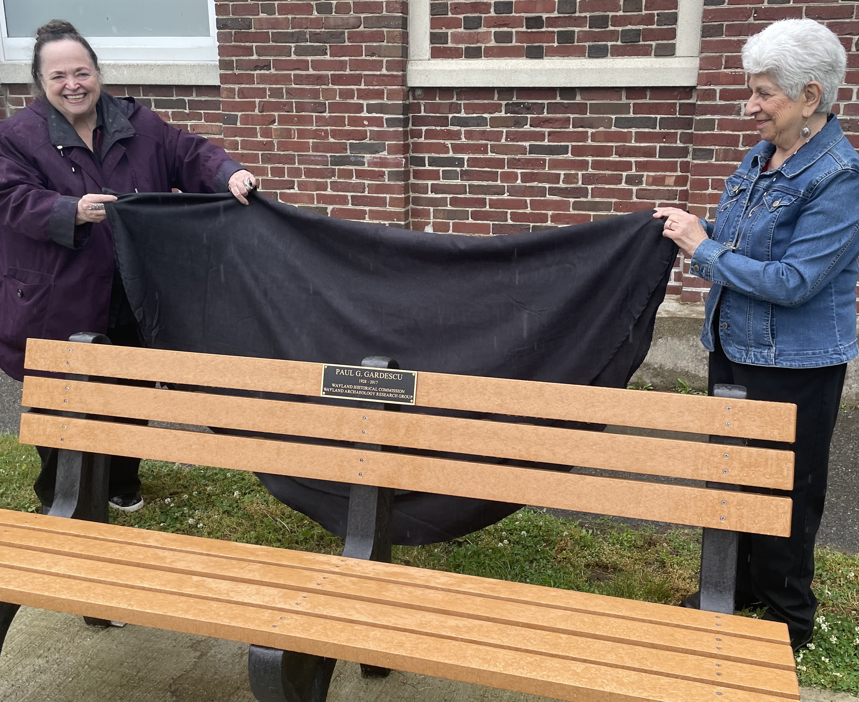 Two women unveiling a bench with a memorial plaque